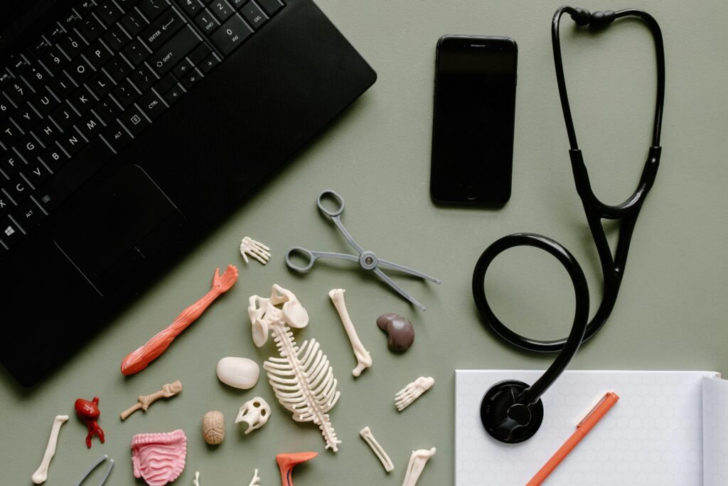 Top view of medical tools, stethoscope, skeleton parts, and laptop on a desk.